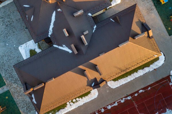 Top aerial view of building brown shingle tiled roof with complex configuration construction. Abstract background, geometrical pattern.